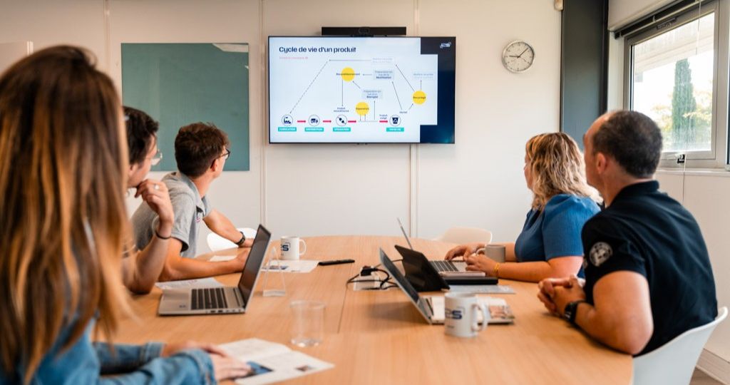 5 personnes regardent des écrans en réunion